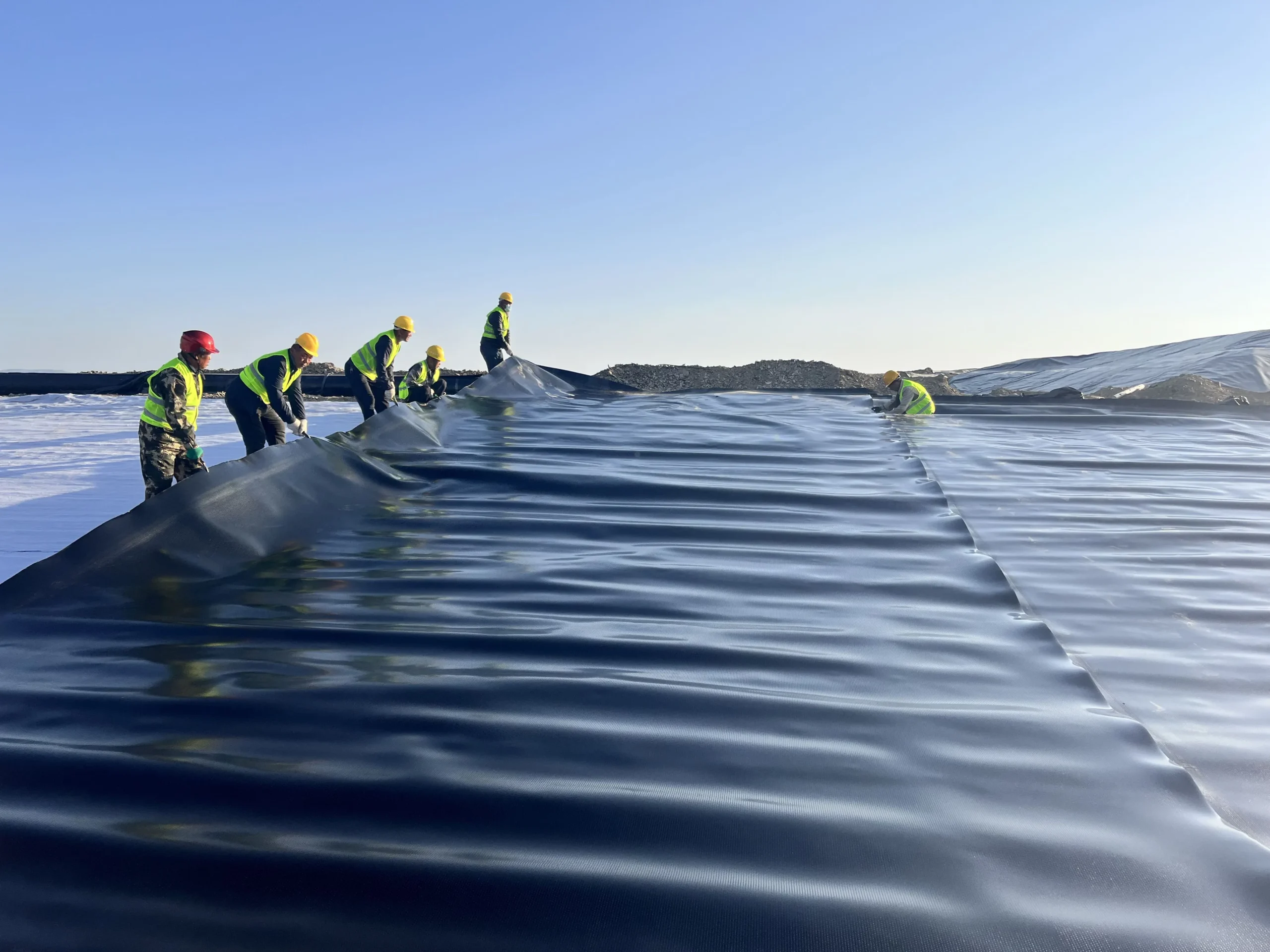 Workers installing a black geomembrane liner at an engineering site